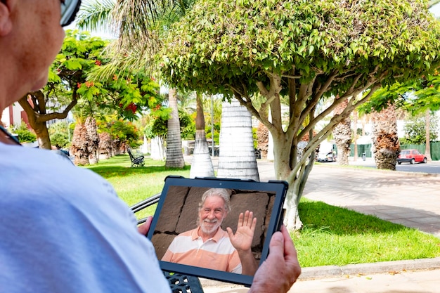 Mujer mayor sentada en un banco en el parque público en video chat con esposo o amigo personas mayores y nuevas tecnologías