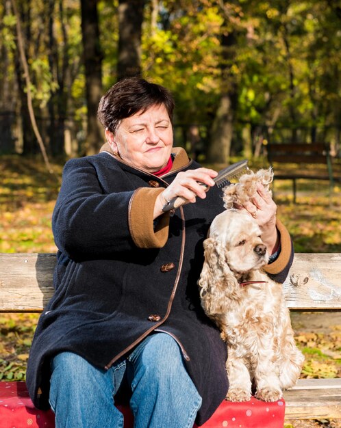 Mujer mayor sentada en un banco con un perro en el parque de otoño