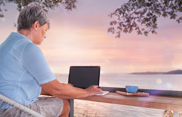 Mujer mayor sentada en un café con vistas al mar y trabajo autónomo