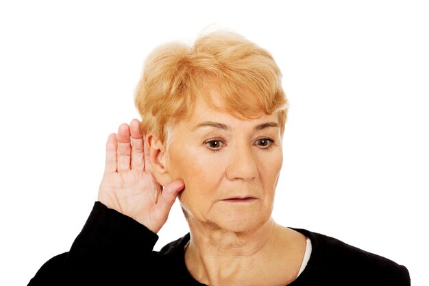 Mujer mayor seria cubriendo la oreja contra un fondo blanco