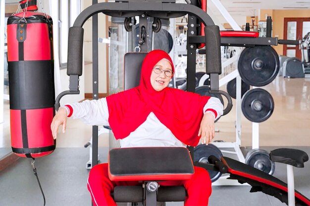 La mujer mayor se sienta en la máquina del gimnasio en el gimnasio