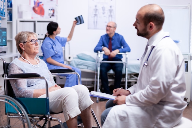 Mujer mayor en silla de ruedas hablando de rehabilitación por discapacidad con el médico en la clínica de recuperación