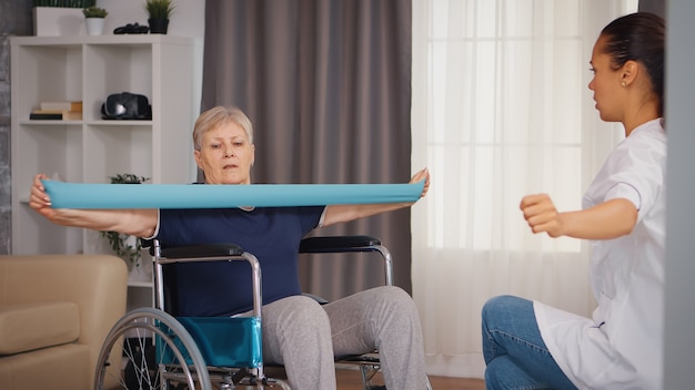 Mujer mayor en silla de ruedas haciendo un tratamiento de rehabilitación con la ayuda de una enfermera. Entrenamiento, deporte, recuperación y levantamiento, asilo de ancianos, enfermería sanitaria, apoyo sanitario, asistencia social