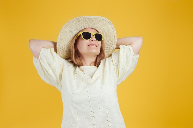 Mujer mayor con sombrero de paja gafas de sol mirando hacia arriba contra el fondo amarillo brillante