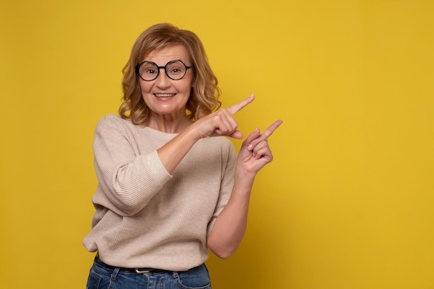 Mujer mayor sonriendo alegremente y señalando con los dedos índices indicando espacio de copia