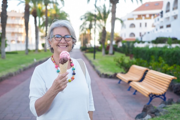 Mujer mayor sonriendo comiendo helado de chocolate y fresa mirando a la cámara Mujer jubilada feliz disfrutando de comida dulce en el parque público