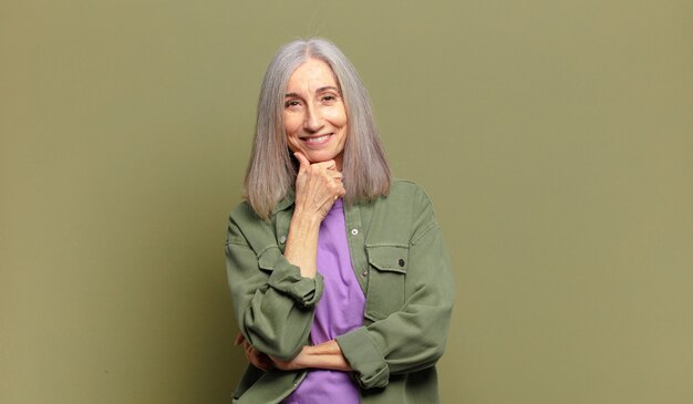 Mujer mayor sonriendo, disfrutando de la vida, sintiéndose feliz, amigable, satisfecho y despreocupado con la mano en la barbilla