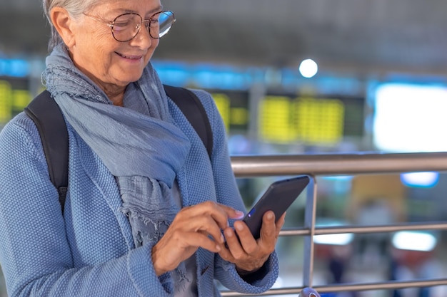 Mujer mayor sonriente en el aeropuerto esperando el embarque mediante conexión de teléfono móvil para enviar mensajes y chatear Concepto de viajero personas con mochila