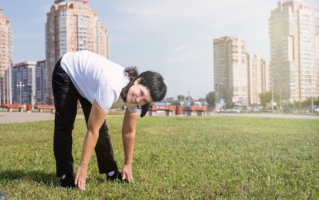 Mujer mayor sonriente calentamiento estirando al aire libre en el parque