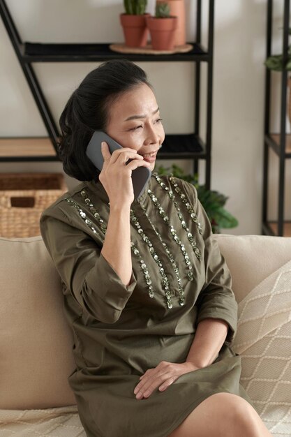 Mujer mayor sonriente y elegante que disfruta hablando por teléfono con un amigo o familiar cuando está sentada en...