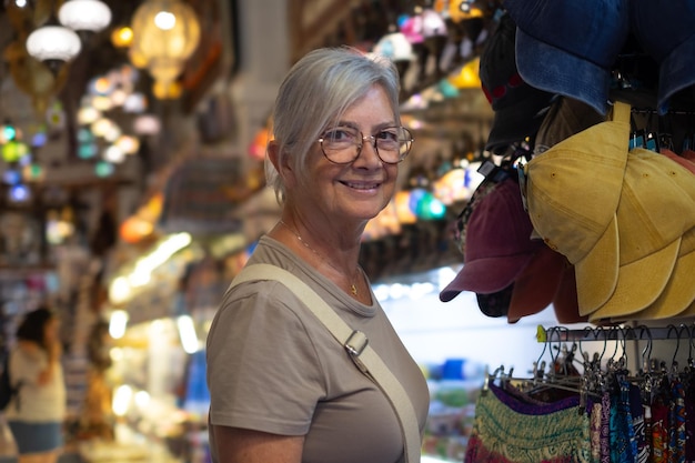 Una mujer mayor sonriente con gafas comprando en una tienda de artículos turísticos