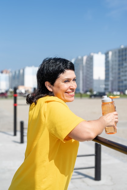 Mujer mayor sonriente que descansan después del entrenamiento al aire libre en las barras del campo de deportes