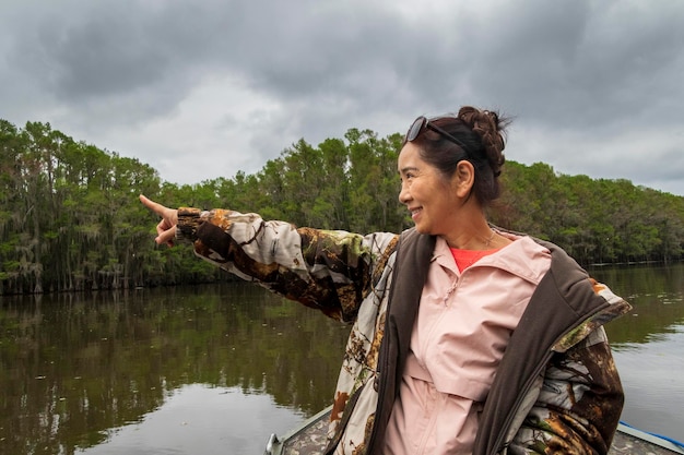 Foto una mujer mayor sonriente señalando mientras está de pie en un barco en el lago