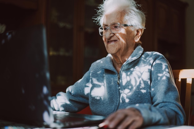 Una mujer mayor sonriente usando una computadora portátil mientras está sentada en casa