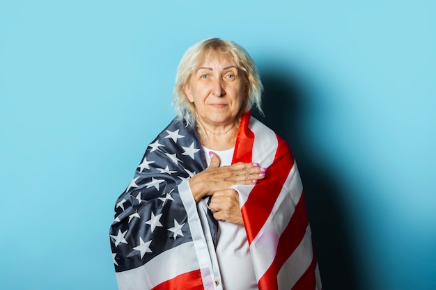 La mujer mayor sostiene la bandera americana en un fondo azul. Concepto de celebración del día de la independencia, día conmemorativo, emigración, bandera estadounidense