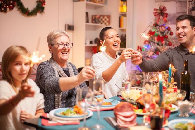 Mujer mayor y su hija riéndose de la celebración de Navidad y sosteniendo los fuegos artificiales de la mano.