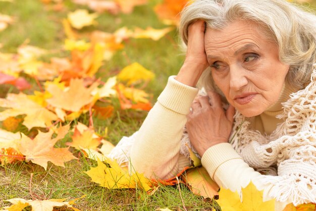 Mujer mayor triste en el parque de otoño