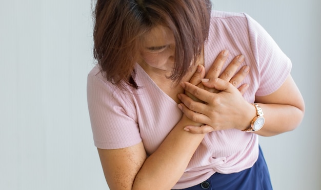 Una mujer mayor usa la mano para hacer un agujero en el pecho con dolor y sufre una enfermedad cardíaca. Concepto de infarto de miocardio con elevación del ST.