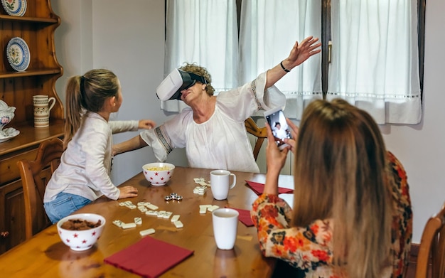 Mujer mayor usando gafas de realidad virtual mientras su hija toma una foto con su móvil
