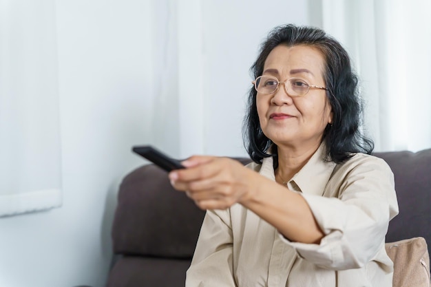 Mujer mayor viendo televisión inteligente y usando el control remoto Mano sosteniendo el control remoto de audio de la televisión Mujer asiática de mediana edad película Serie de televisión pasando tiempo en casa