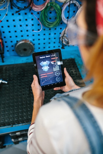 Foto mujer mecánica comprobando la aplicación de diagnóstico del motor en una tableta digital