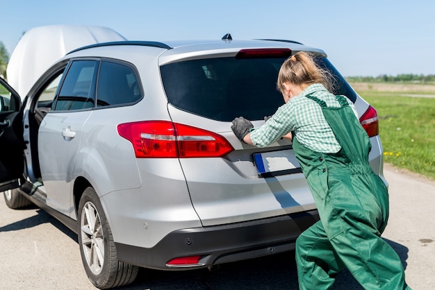 Mujer mecánico empujando coche roto en la carretera