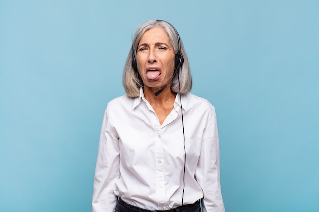 Mujer de mediana edad con actitud alegre, despreocupada, rebelde, bromeando y sacando la lengua, divirtiéndose. concepto de telemarketer