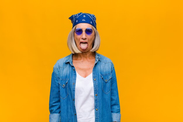 Mujer de mediana edad con actitud alegre, despreocupada y rebelde, bromeando y sacando la lengua, divirtiéndose