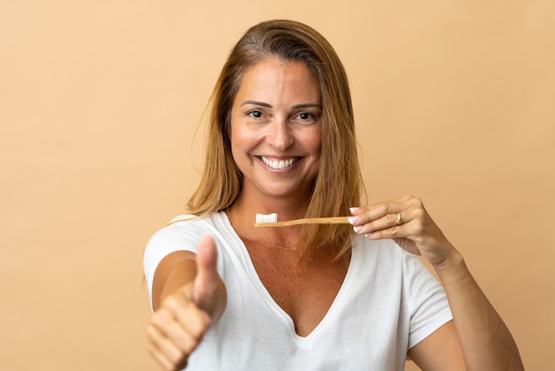 Mujer de mediana edad aislada en la pared beige con un cepillo de dientes