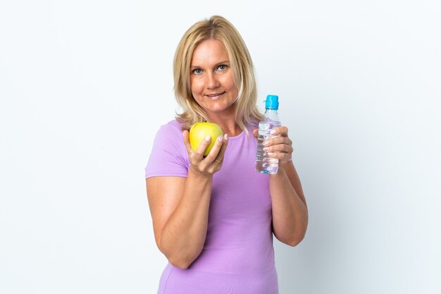 Mujer de mediana edad aislada en la pared blanca con una manzana y con una botella de agua