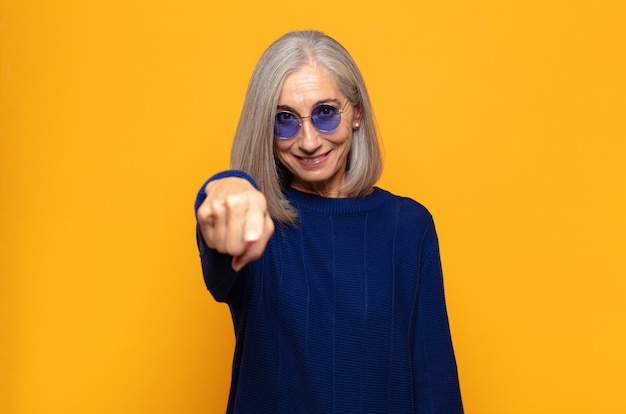 Mujer de mediana edad apuntando con una sonrisa satisfecha, confiada y amistosa, eligiéndote