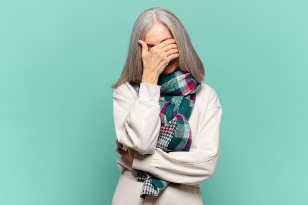 Mujer de mediana edad con aspecto estresado, avergonzado o molesto, con dolor de cabeza, cubriéndose la cara con la mano