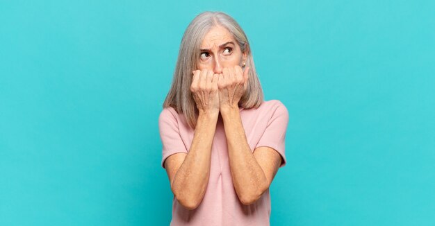 Mujer de mediana edad con aspecto preocupado, ansioso, estresado y asustado, mordiéndose las uñas y mirando al espacio de copia lateral