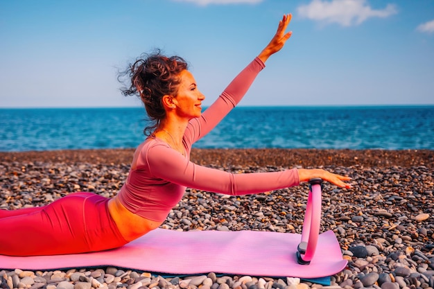 Mujer de mediana edad bien parecido con cabello negro haciendo pilates con el anillo en la estera de yoga cerca de la