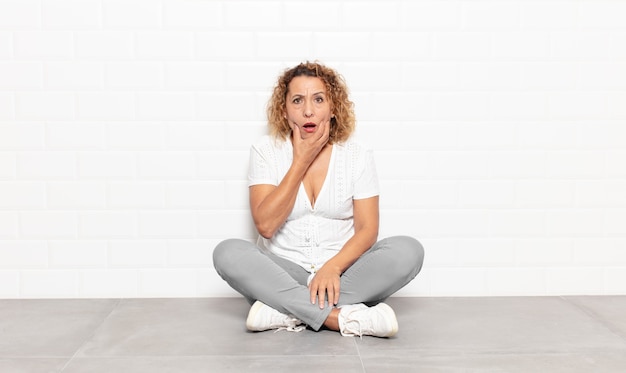 Mujer de mediana edad con la boca y los ojos bien abiertos y la mano en la barbilla, sintiéndose desagradablemente conmocionada, diciendo qué o guau