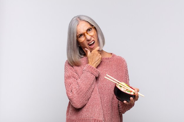 Mujer de mediana edad con la boca y los ojos bien abiertos y la mano en el mentón