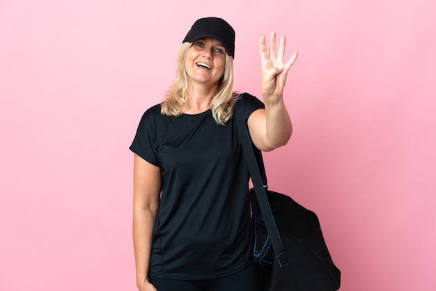 Foto mujer de mediana edad con bolsa de deporte aislada en rosa feliz y contando cuatro con los dedos