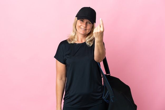 Mujer de mediana edad con bolsa de deporte aislada en rosa haciendo gesto de venida