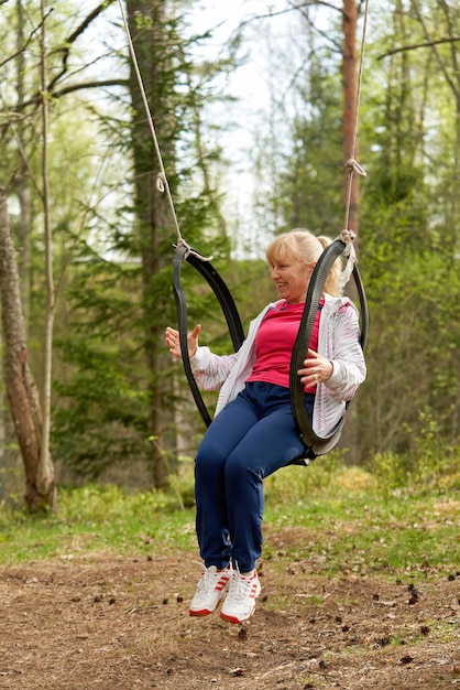 Mujer de mediana edad en el bosque columpiándose en un columpio hecho con un neumático viejo