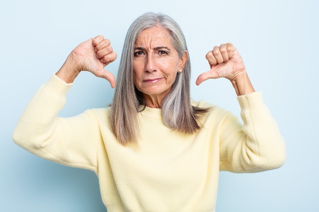 Mujer de mediana edad con cabello gris que parece triste, decepcionada o enojada, mostrando el pulgar hacia abajo en desacuerdo, sintiéndose frustrada