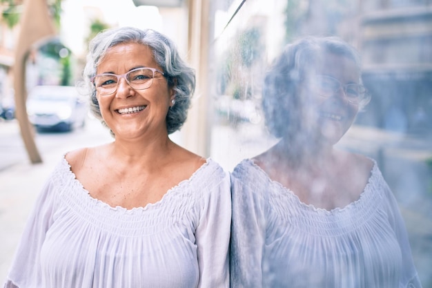 Mujer de mediana edad con cabello gris sonriendo feliz al aire libre