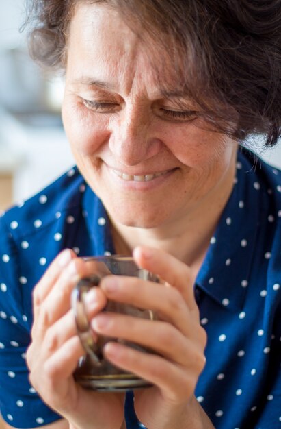 Una mujer de mediana edad en el café sostiene una taza de té caliente en sus manos.