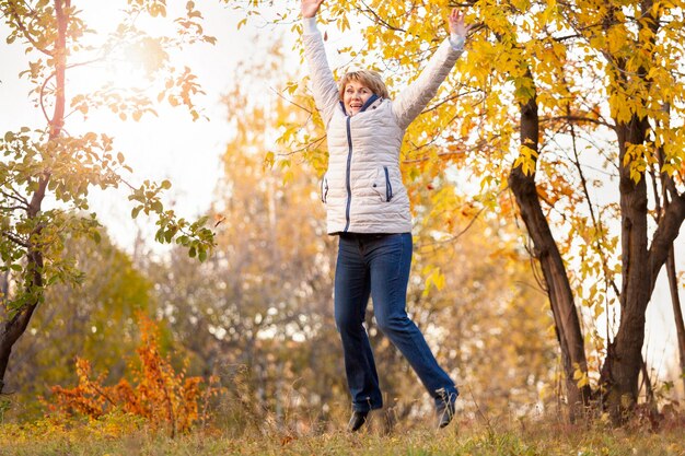 Una mujer de mediana edad camina en el parque de otoño entre los árboles