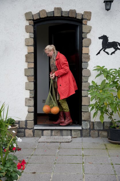 Una mujer de mediana edad con una capa roja con una red de calabazas naranjas abre la puerta