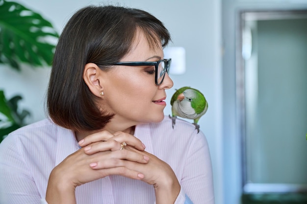 Mujer de mediana edad en casa con un loro mascota en el hombro