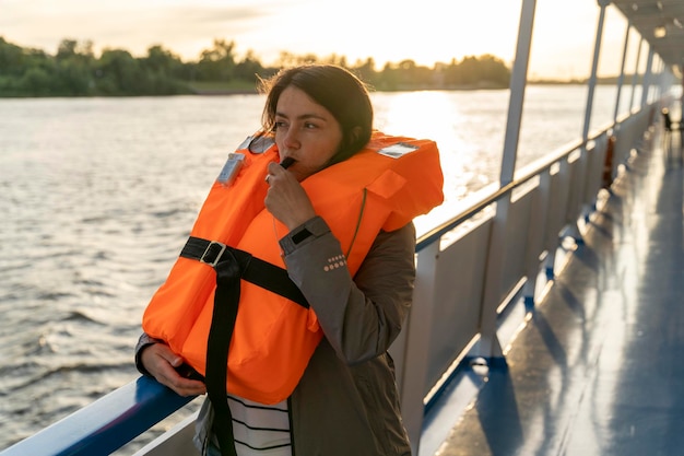 Una mujer de mediana edad con un chaleco salvavidas naranja sopla un silbato la niña da una señal de peligro o da una orden con un silbado un taladro de seguridad en el agua