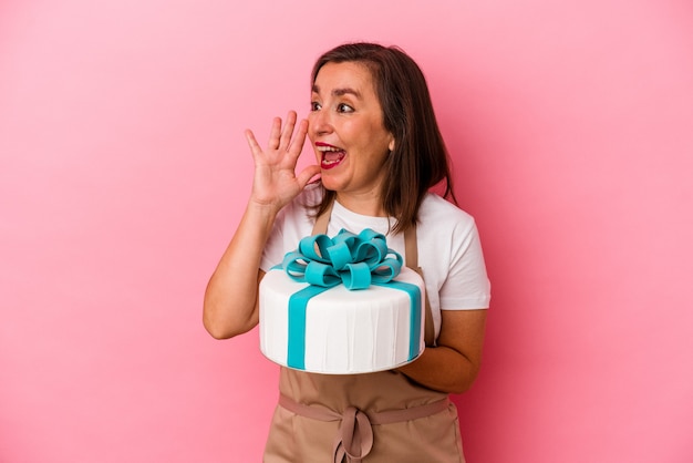 Mujer de mediana edad chef de repostería sosteniendo un pastel aislado sobre fondo azul gritando y sosteniendo la palma cerca de la boca abierta.