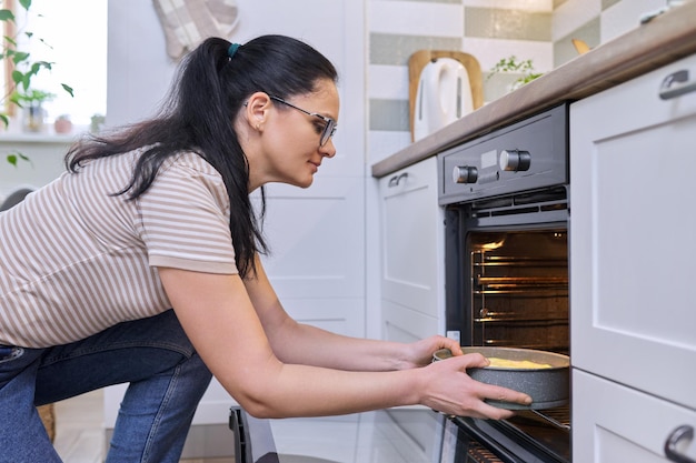 Mujer de mediana edad cocinando pastel en el horno en casa en la cocina