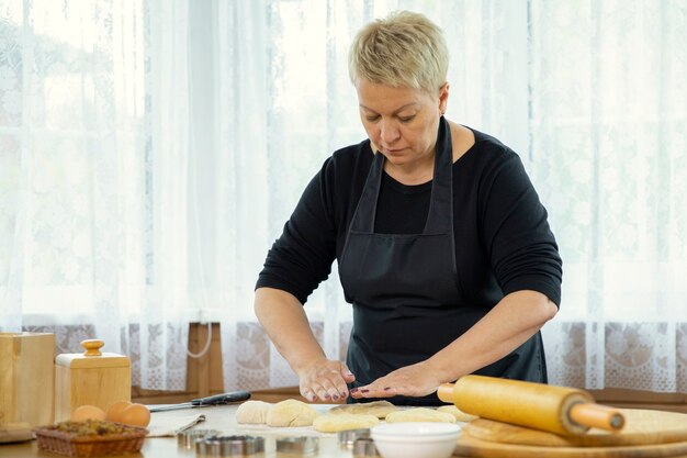 Mujer de mediana edad en delantal negro haciendo galletas caseras