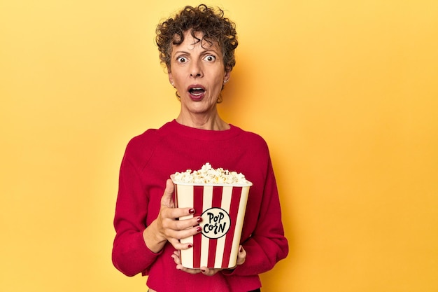 Mujer de mediana edad disfrutando de palomitas de maíz para una película sobre un fondo de estudio amarillo